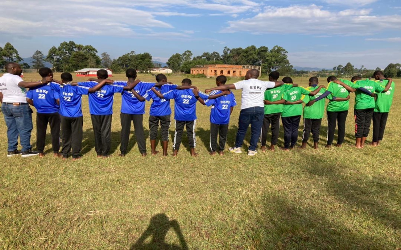 Young people in blue and green jerseys standing in a line on a field, arms around one another